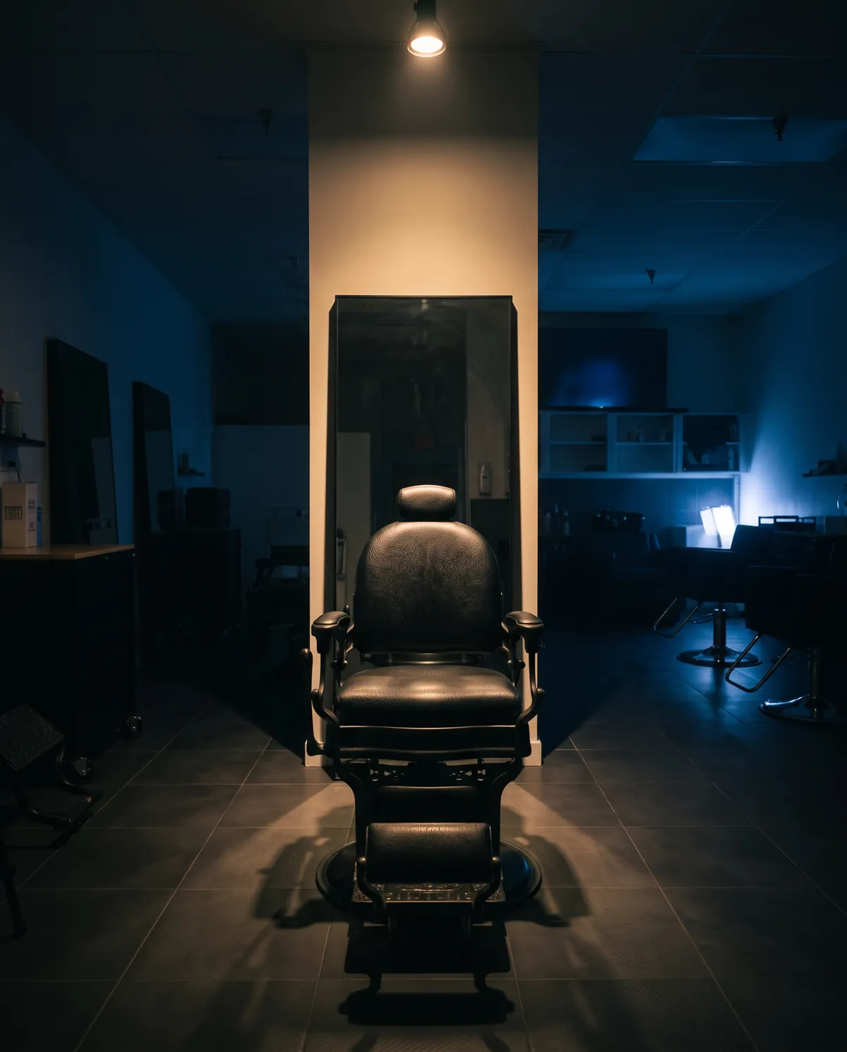 A black barber chair under a single light at No.7 Barber Lounge after hours